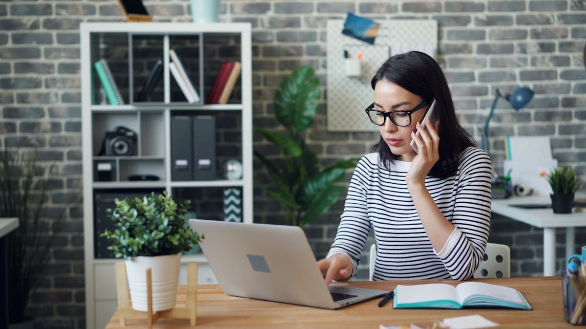 Woman on phone at laptop with notebook in office - Record research calls with RECAP